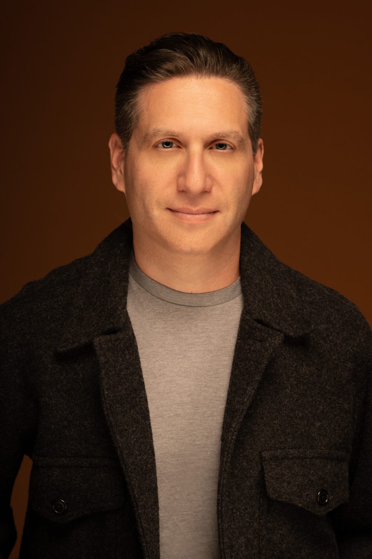 Shai Korman, smiling, in a warm-lit studio portrait